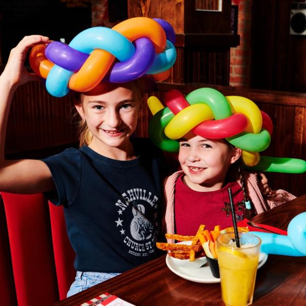 Two children in a restaurant with balloon hats on